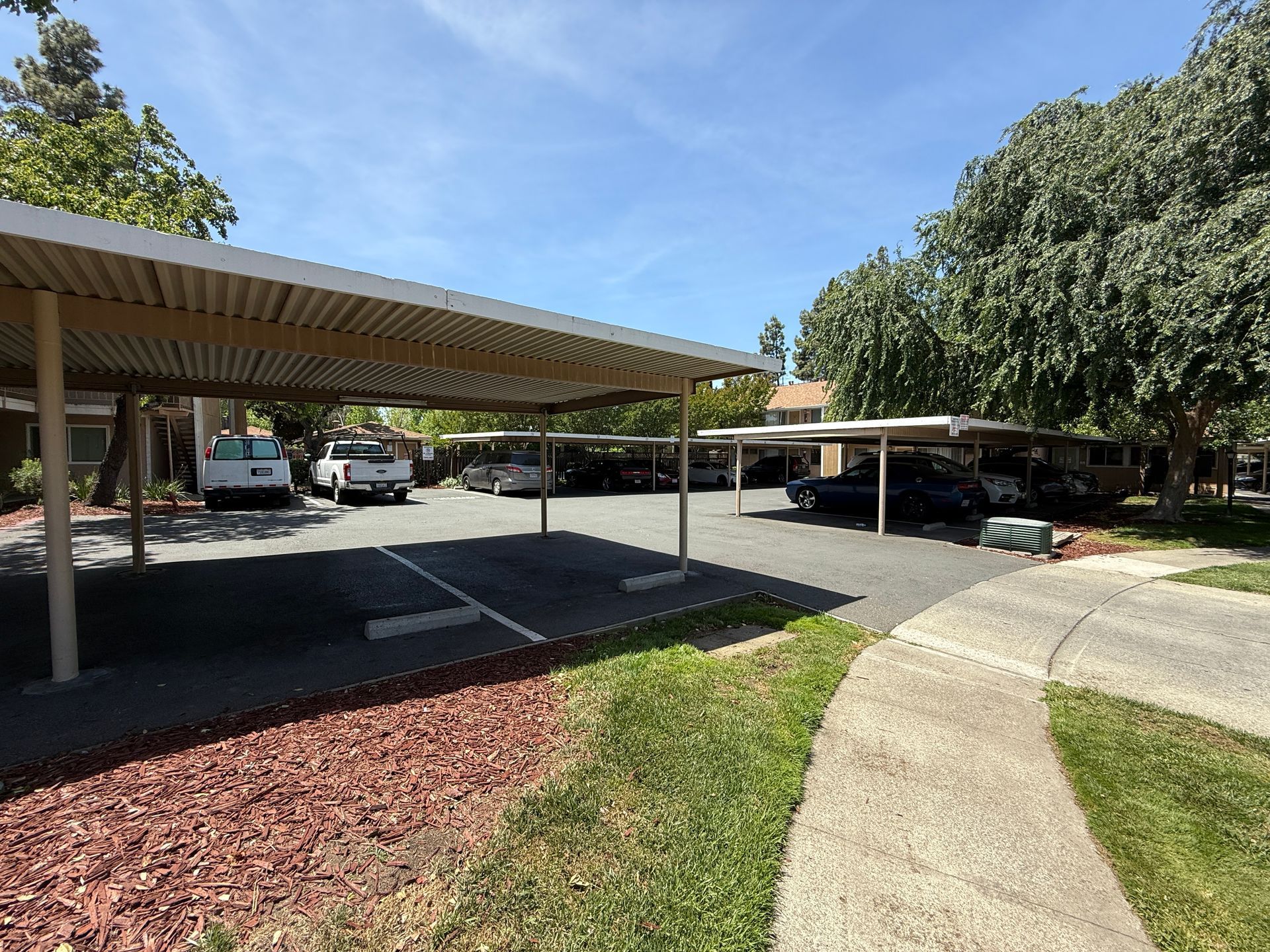 Parking lot with covered carports and vehicles, under a blue sky.