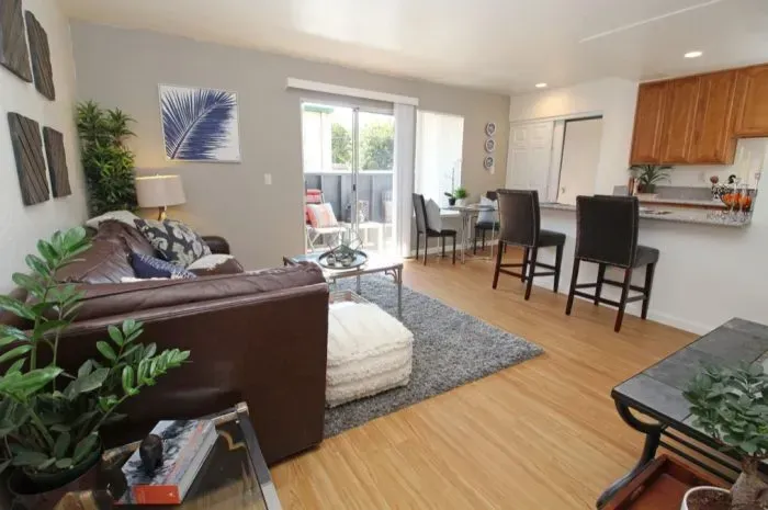 Cozy living room with brown leather sofa, open to kitchen and small outdoor patio.