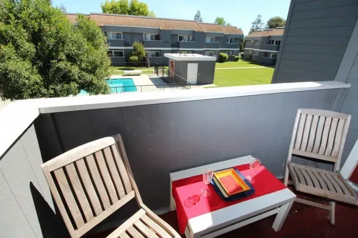 Balcony with two wooden chairs and a table overlooking a pool and apartment buildings.