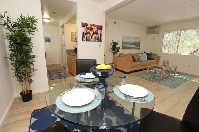 Living room with dining area, brown sofa, glass table, blue accents, light wood floor.
