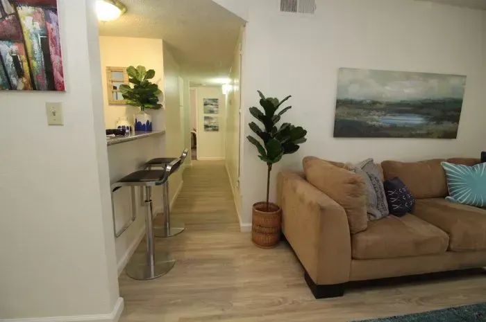 Living room with a tan couch, plant, bar, and hallway.