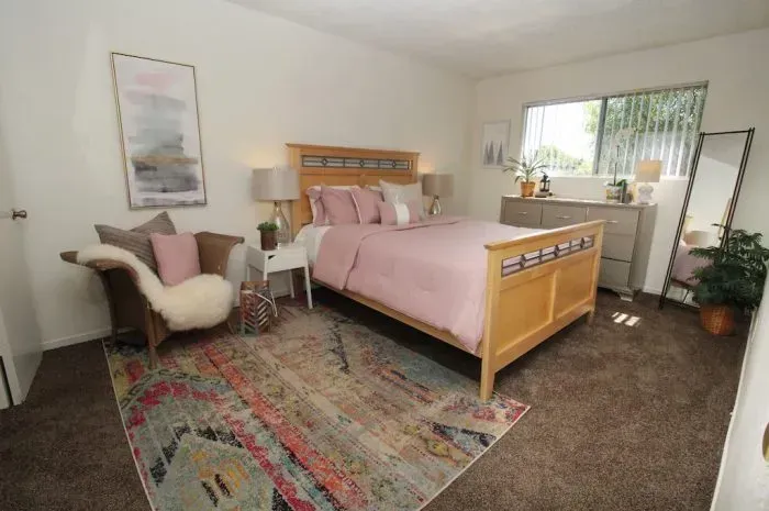 Bedroom with a bed, chair, rug, dresser, and mirror, decorated in shades of pink and beige.