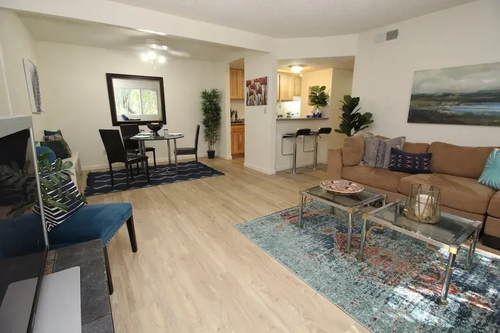 Living room and dining area with brown sofa, blue rugs, and light wood flooring.