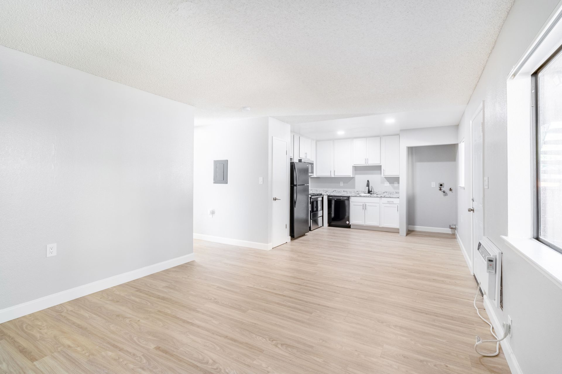 Bright white apartment interior with kitchen, light wood floors, and large window.