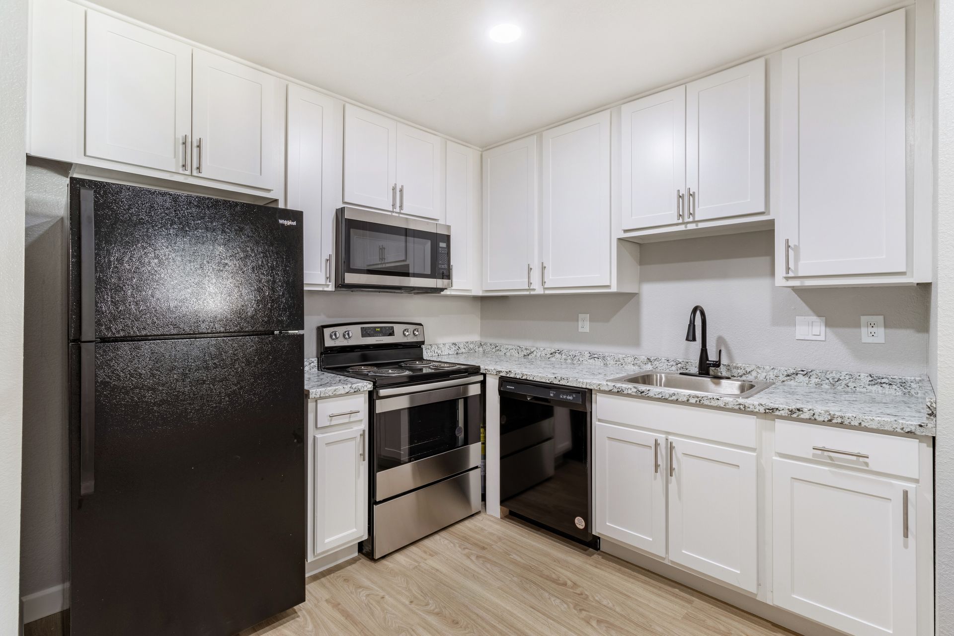White kitchen with stainless steel appliances, white cabinets, and light wood-look flooring.