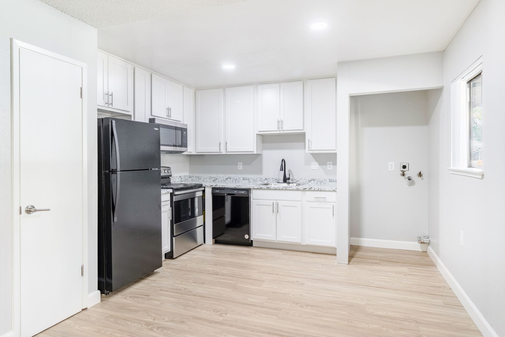 Bright kitchen with white cabinets, black appliances, and light wood-look flooring.