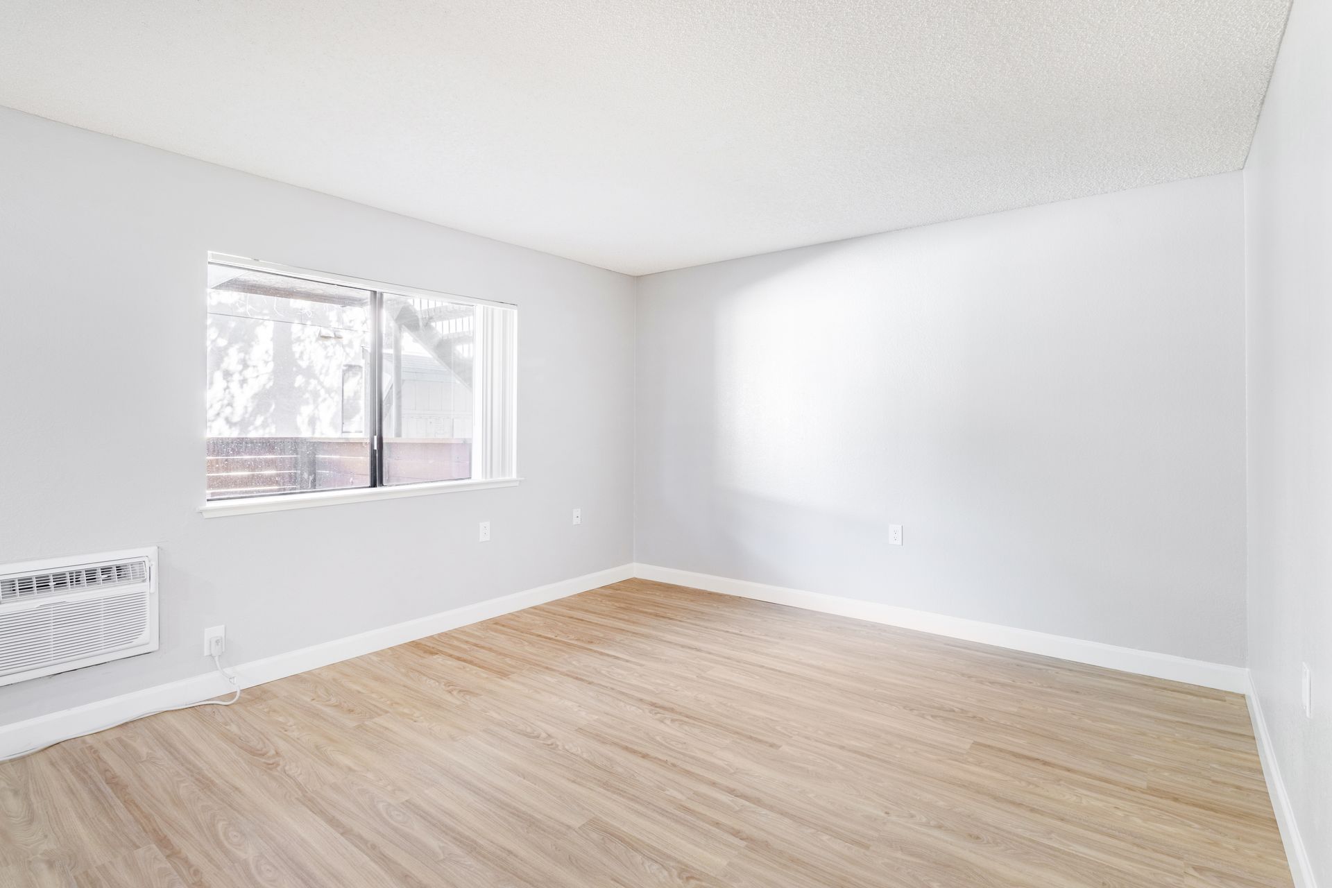 Empty, pale gray room with window and light wood flooring.