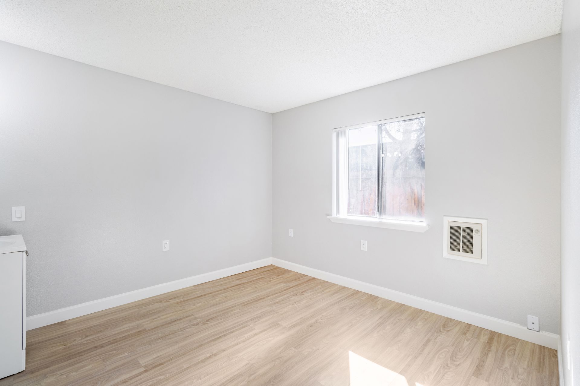 Empty room with light wood floor, gray walls, and a window.