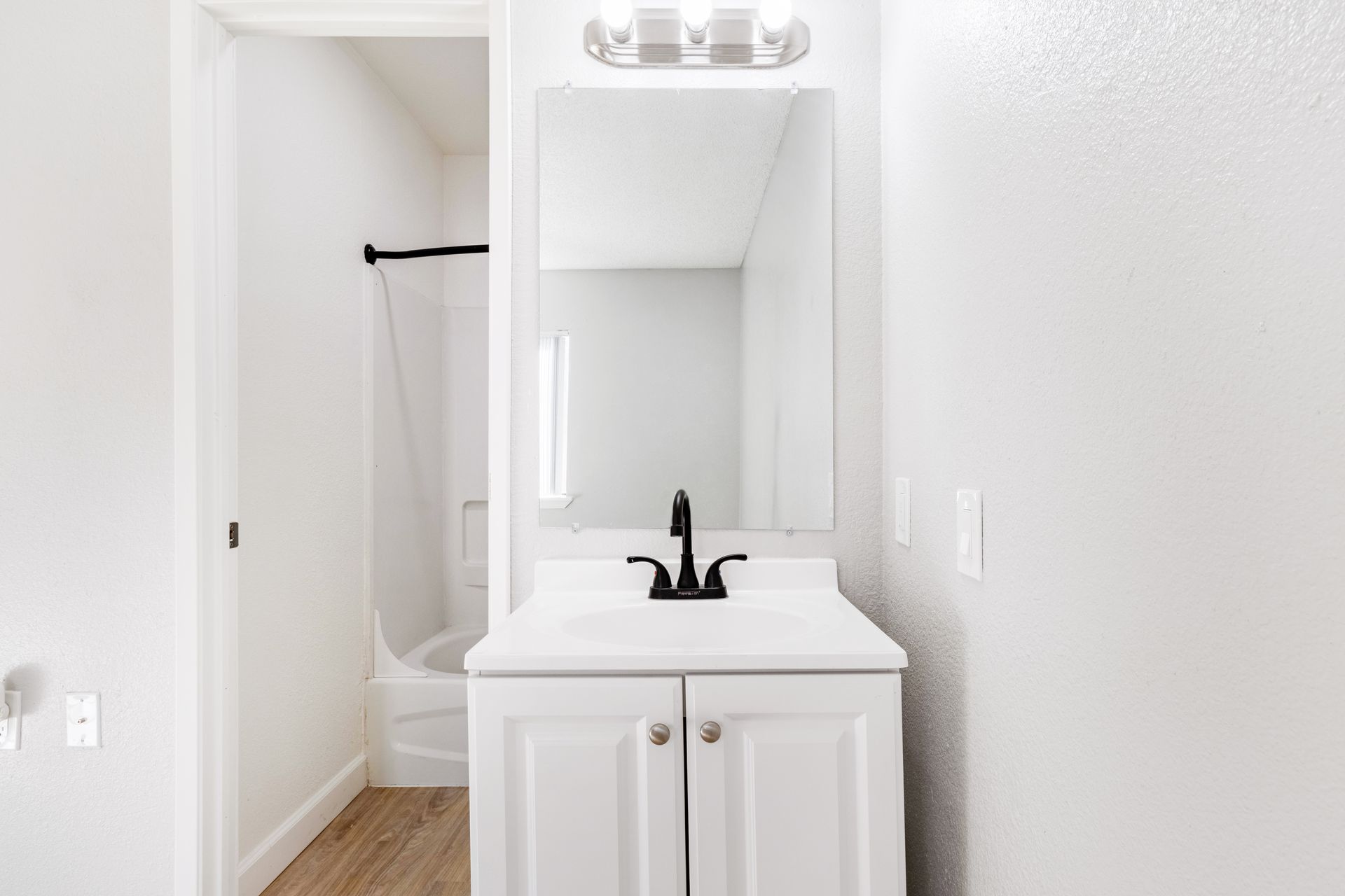 White bathroom with vanity, mirror, and a view into a shower.