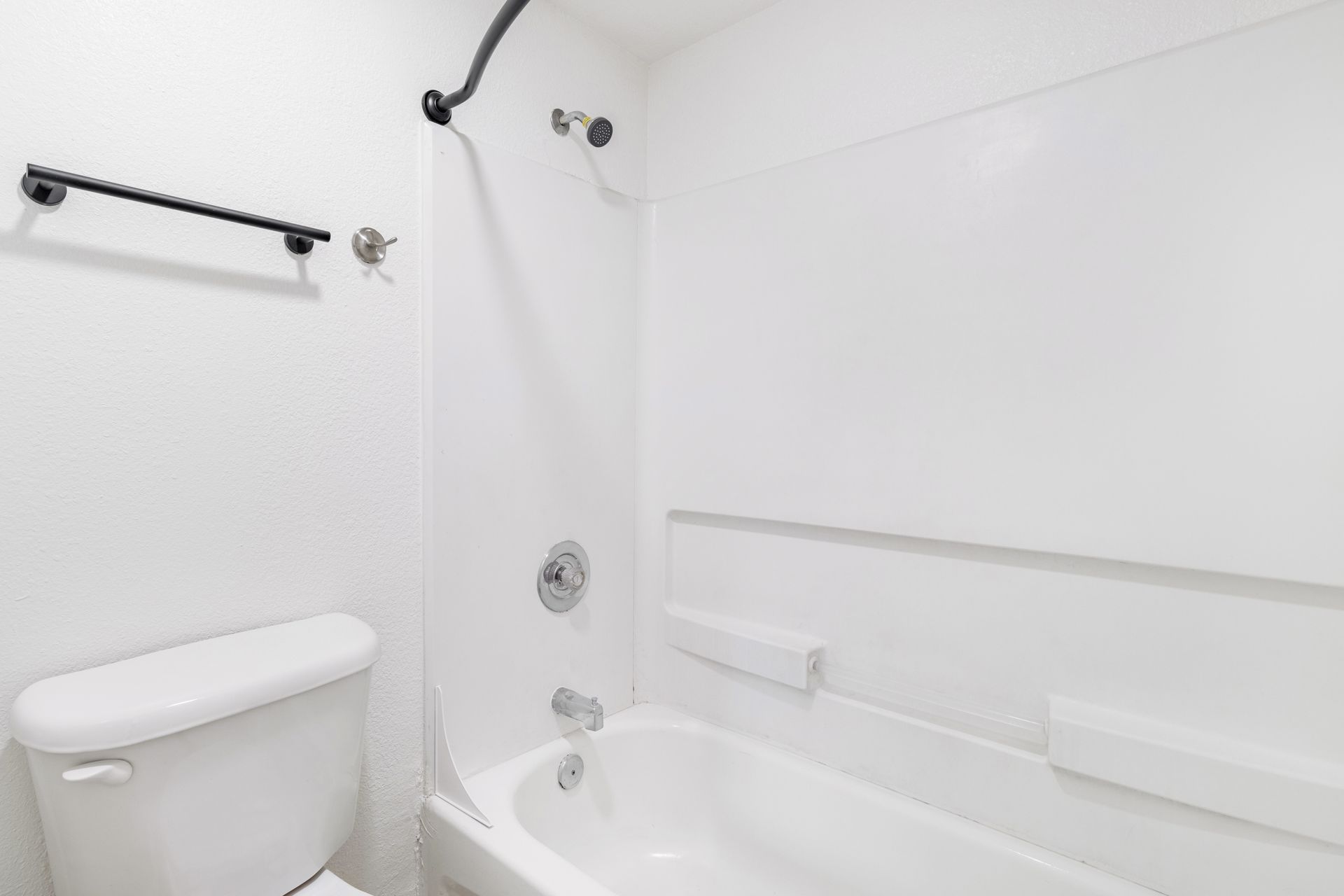 White bathroom with toilet, bathtub, shower, and towel rack.