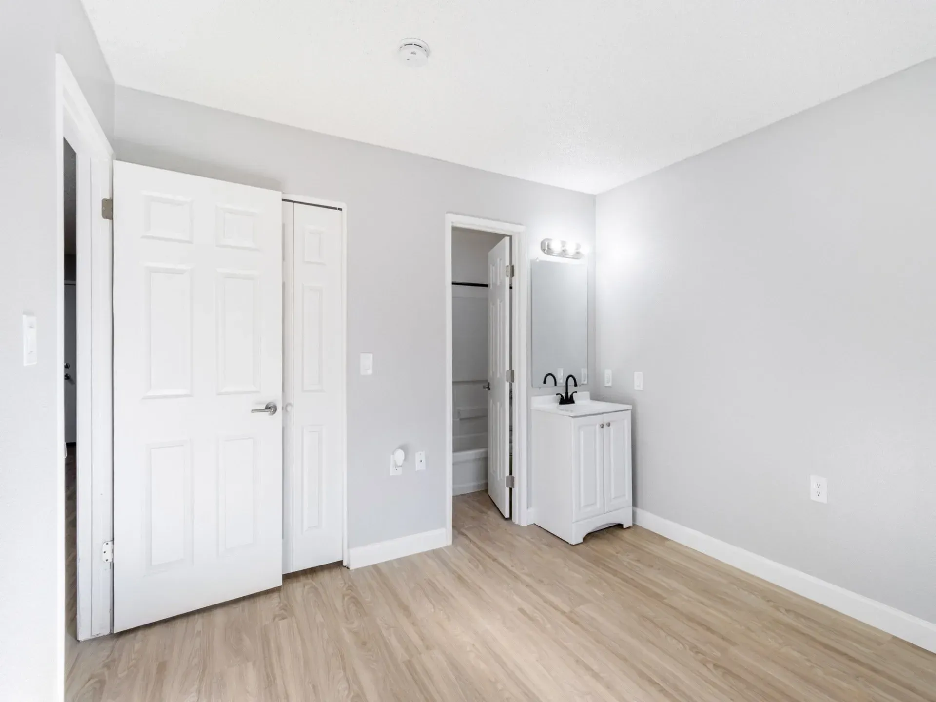 Bedroom with light wood flooring, white doors, and a bathroom entrance.