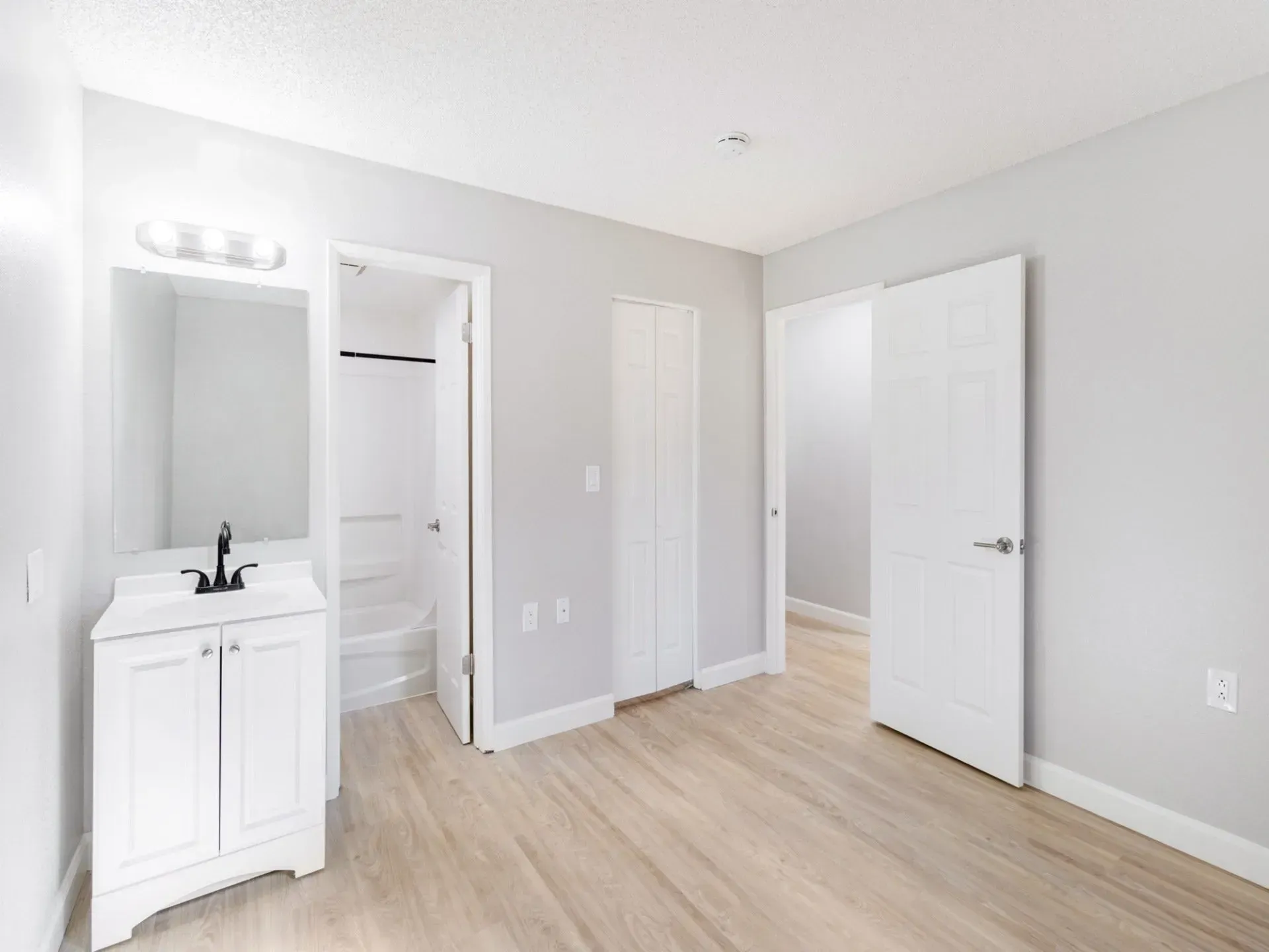 Bathroom with white vanity, door to shower, closed door, and light wood flooring.