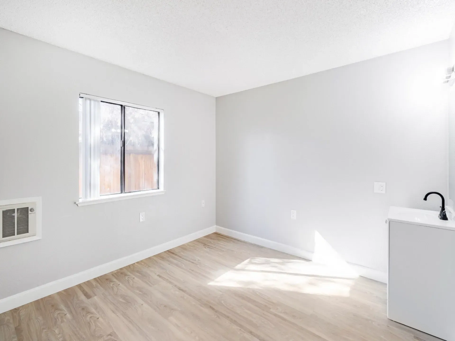 Empty room with gray walls, window, and light wood flooring.