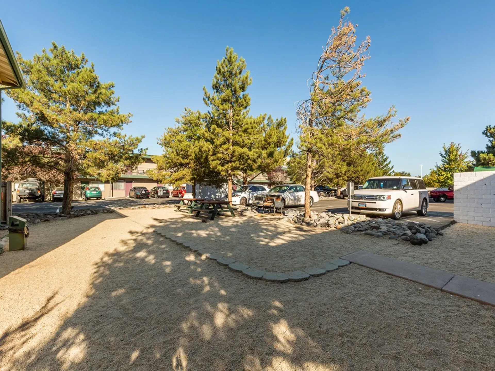 Parking area with gravel, cars, and trees under a clear blue sky.