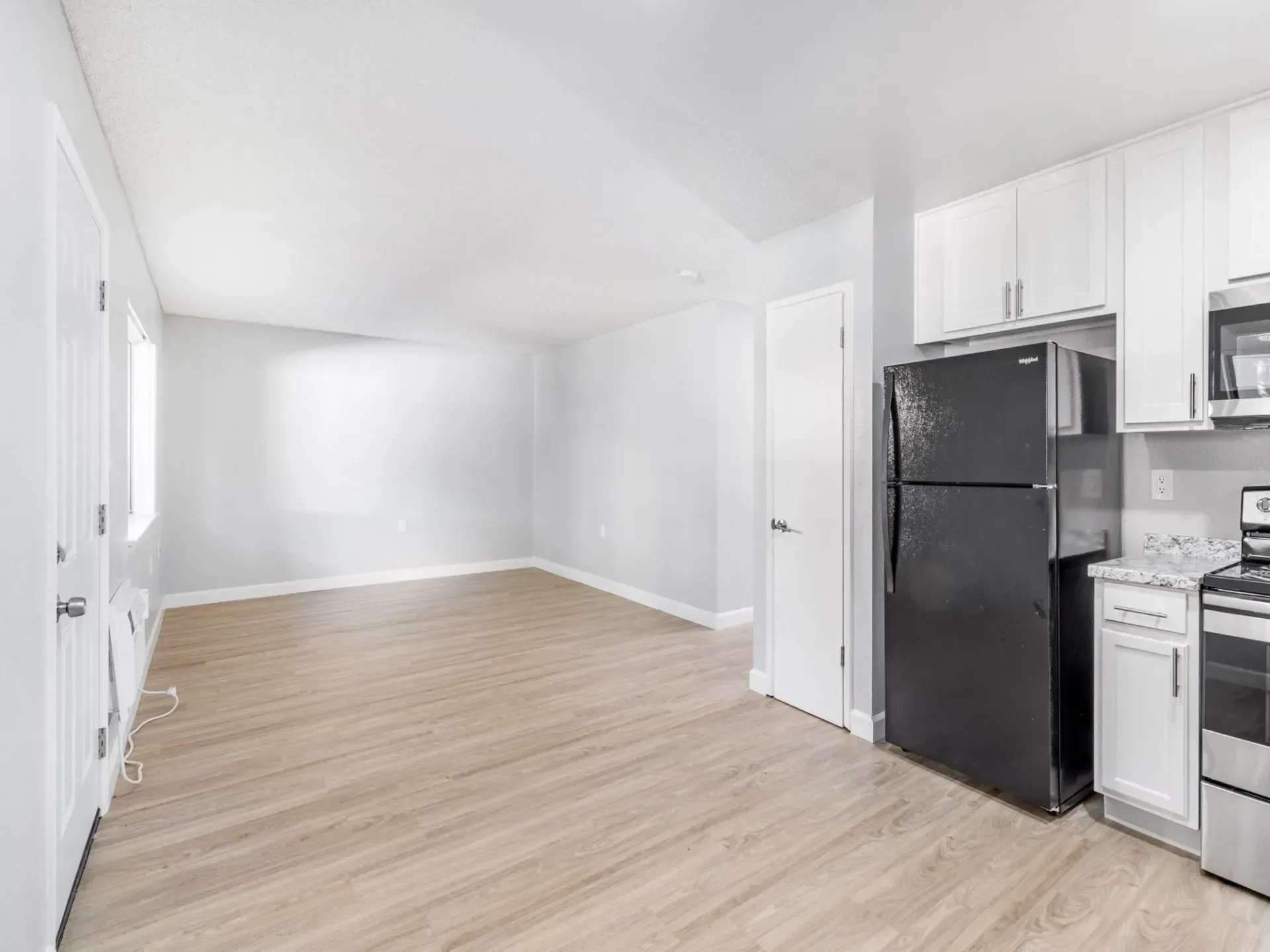 Empty apartment interior with kitchen, black refrigerator, and wood-look flooring.