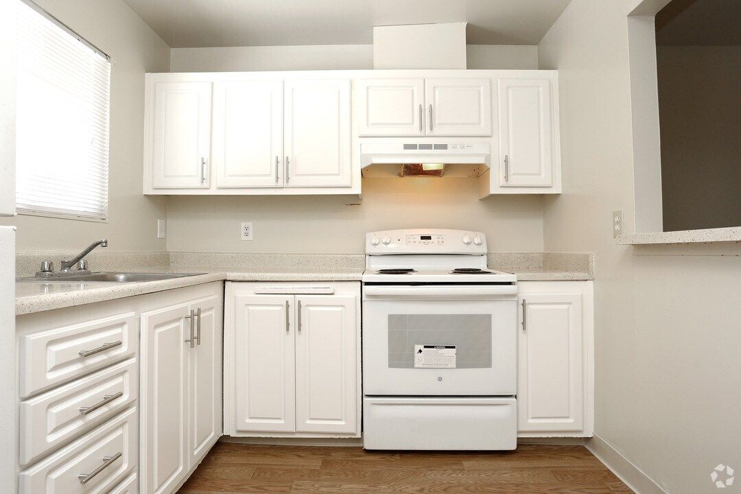 White kitchen with white cabinets, countertops, and appliances.  A window is on the left, and a range hood above the stove.