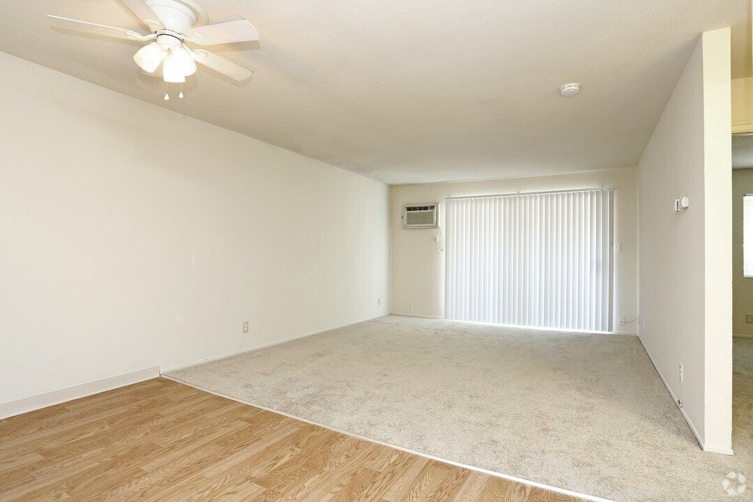 Empty living room with beige carpet, sliding doors, and ceiling fan.