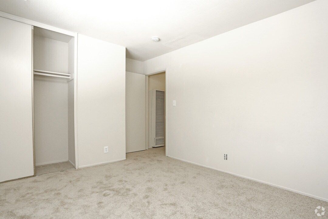Empty, carpeted room with closet, painted white walls, and a thermostat.