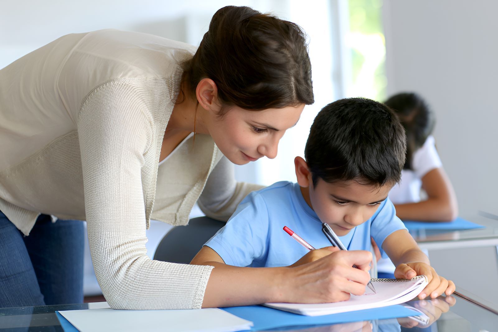A Woman is Helping a Young Boy With His Homework — Newcastle Paediatric Occupational Therapy In Floraville, NSW