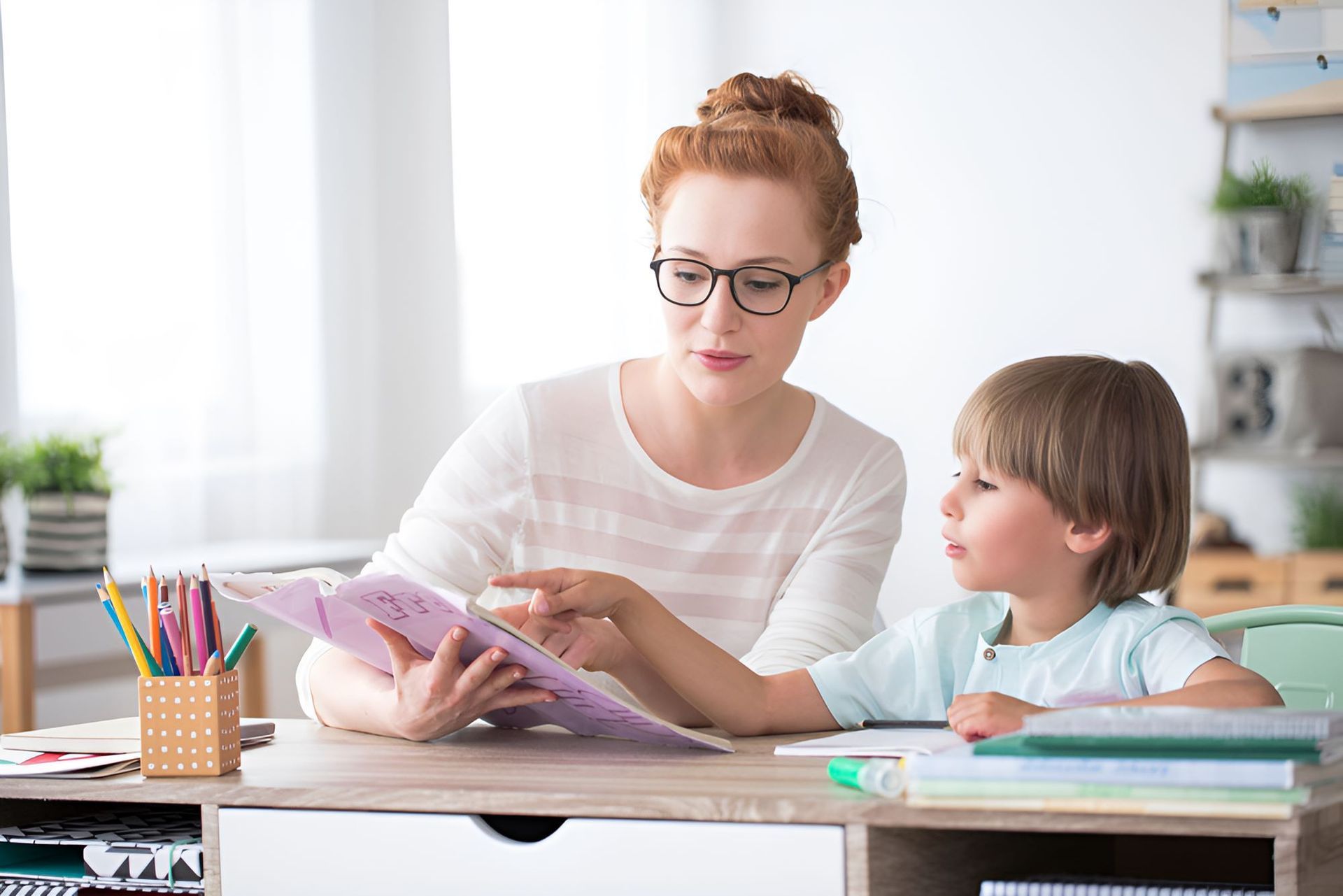 A Woman is Helping a Young Boy With His Homework — Newcastle Paediatric Occupational Therapy in Belmont, NSW