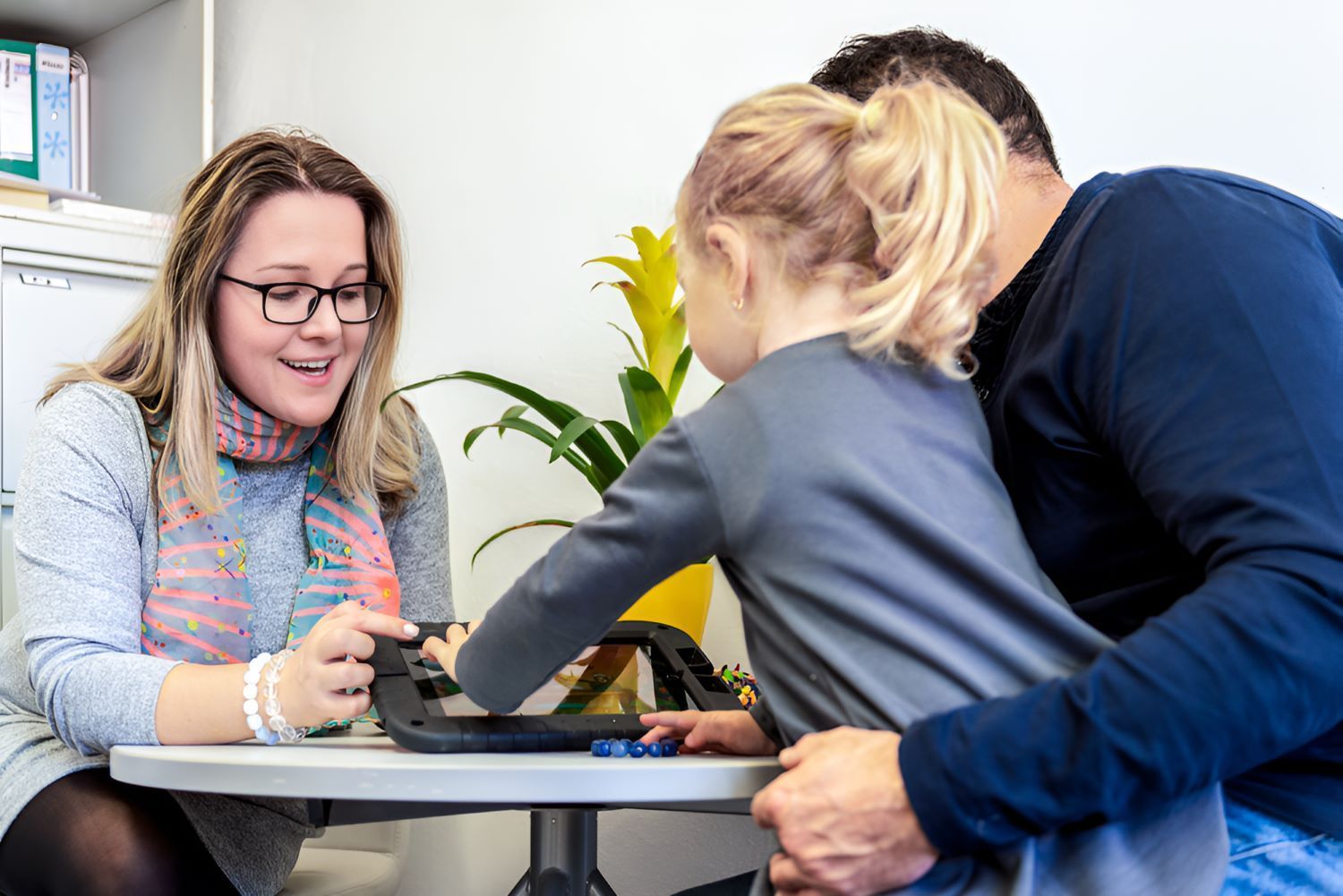 A Man and a Woman Are Sitting at a Table With a Little Girl — Newcastle Paediatric Occupational Therapy in Belmont, NSW