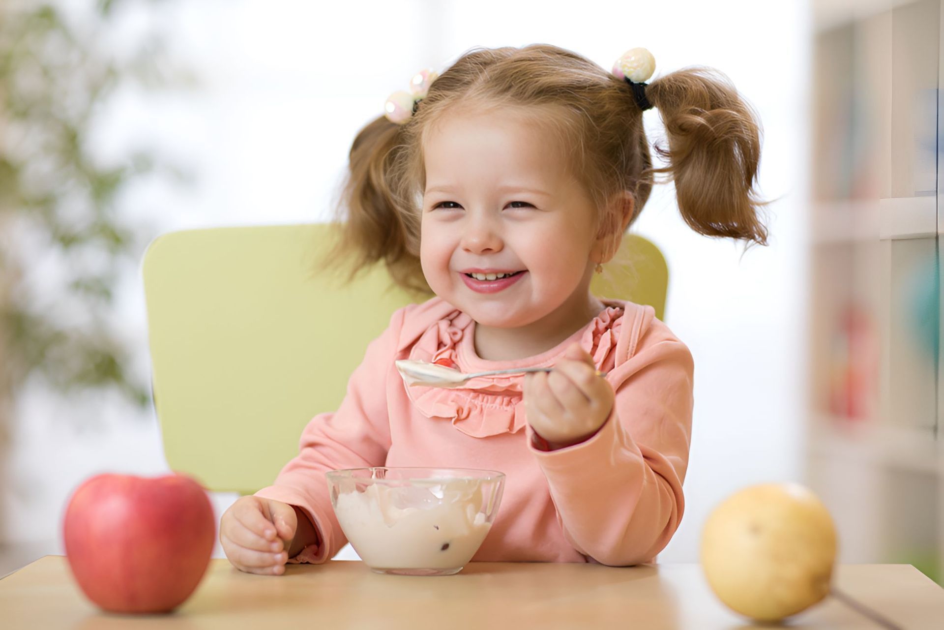 A Little Girl is Sitting at a Table Eating Yogurt — Newcastle Paediatric Occupational Therapy in Floraville, NSW