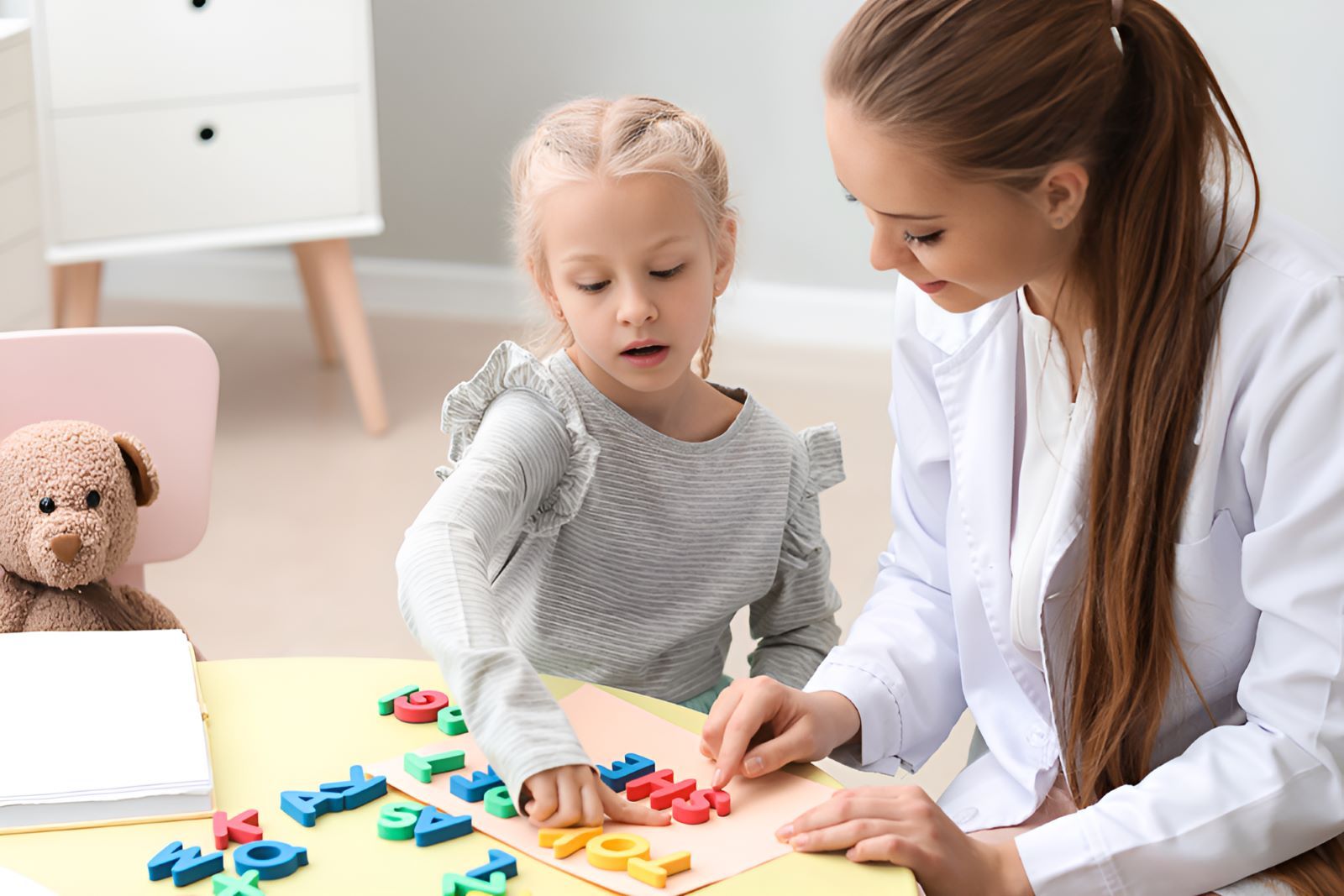 A Woman is Teaching a Little Girl How to Read Letters — Newcastle Paediatric Occupational Therapy in Mayfield, NSW