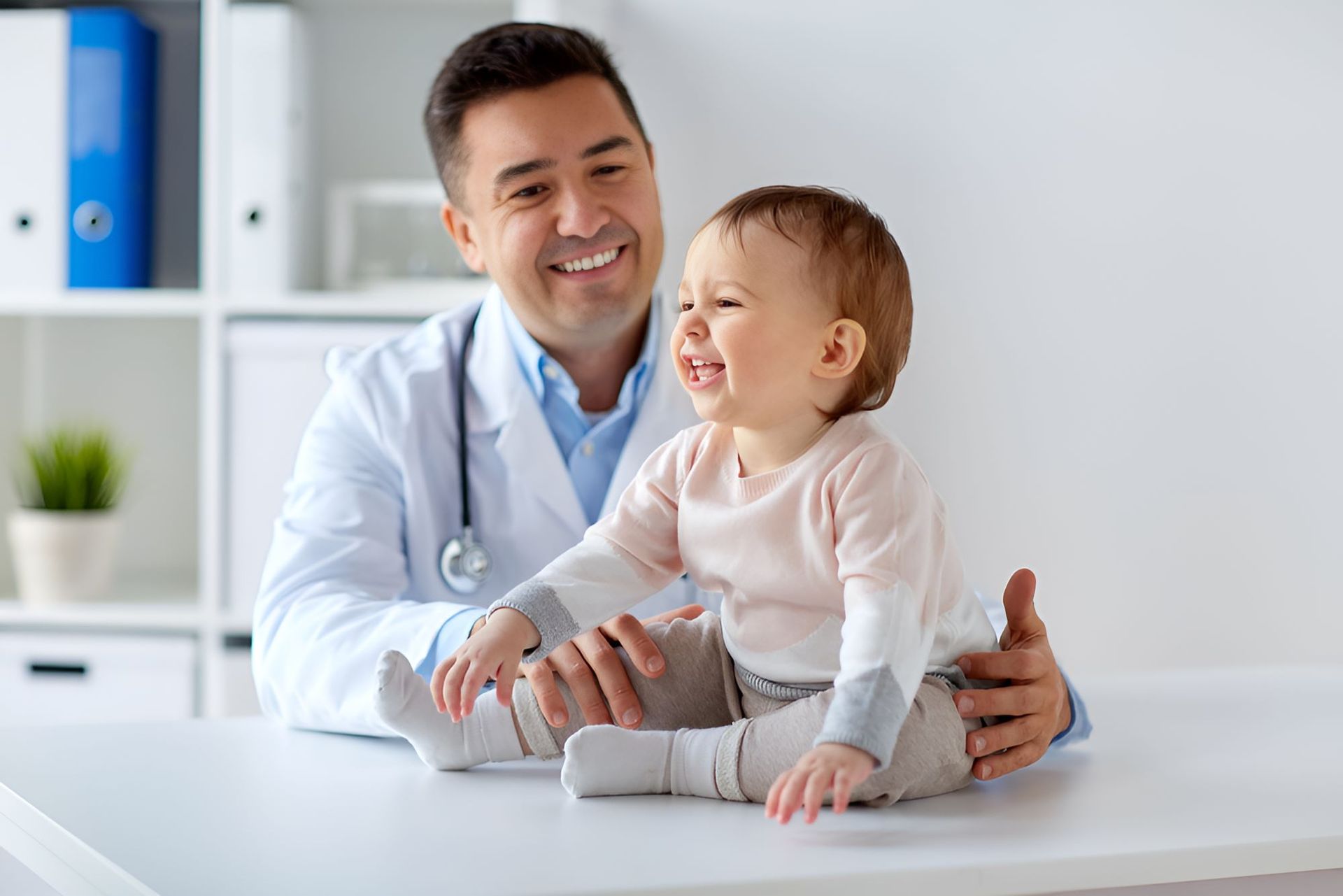 A Doctor is Holding a Baby Girl Who is Sitting on a Table — Newcastle Paediatric Occupational Therapy in Newcastle, NSW