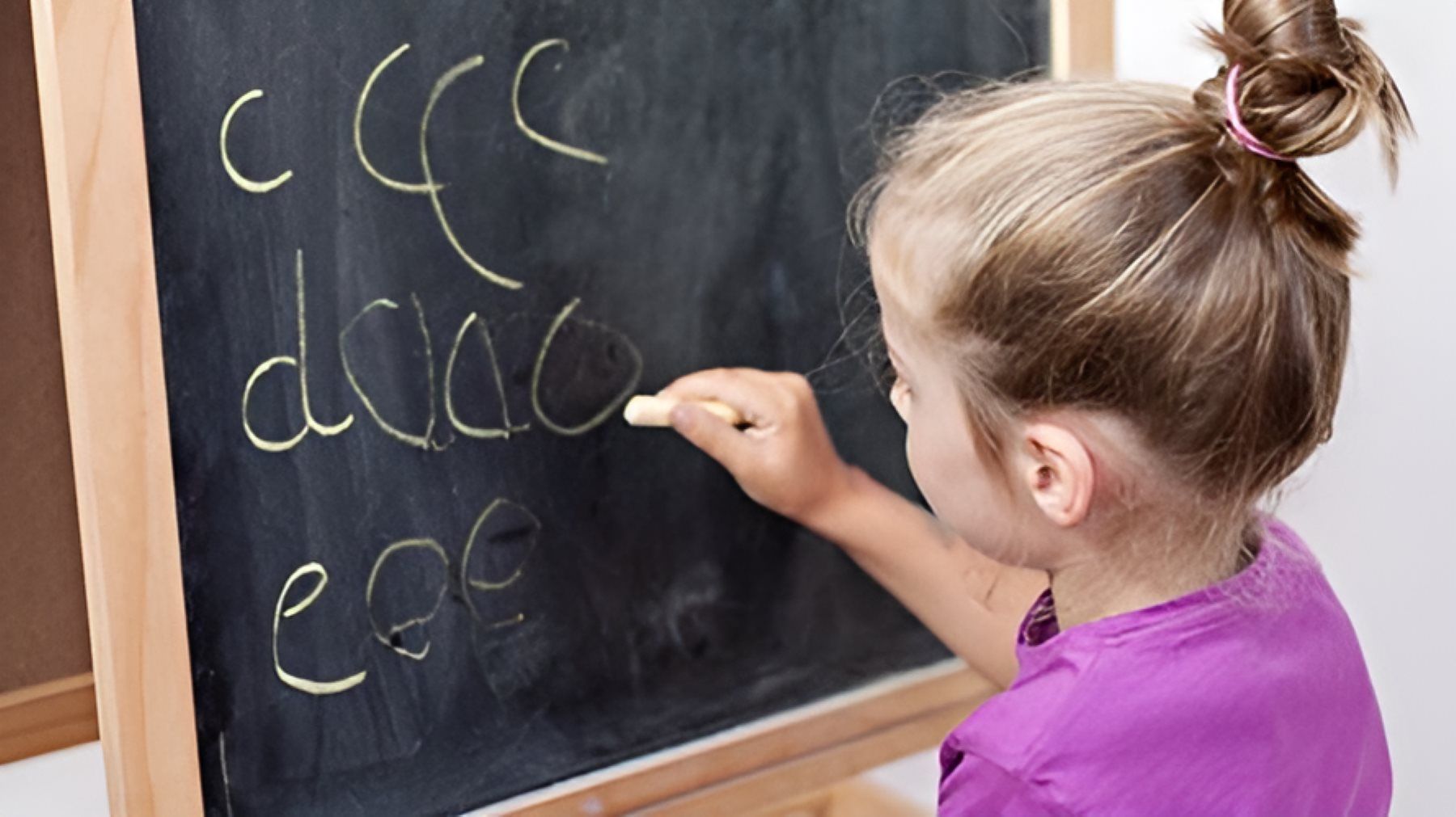 A Little Girl is Writing on a Blackboard With Chalk — Newcastle Paediatric Occupational Therapy in Floraville, NSW