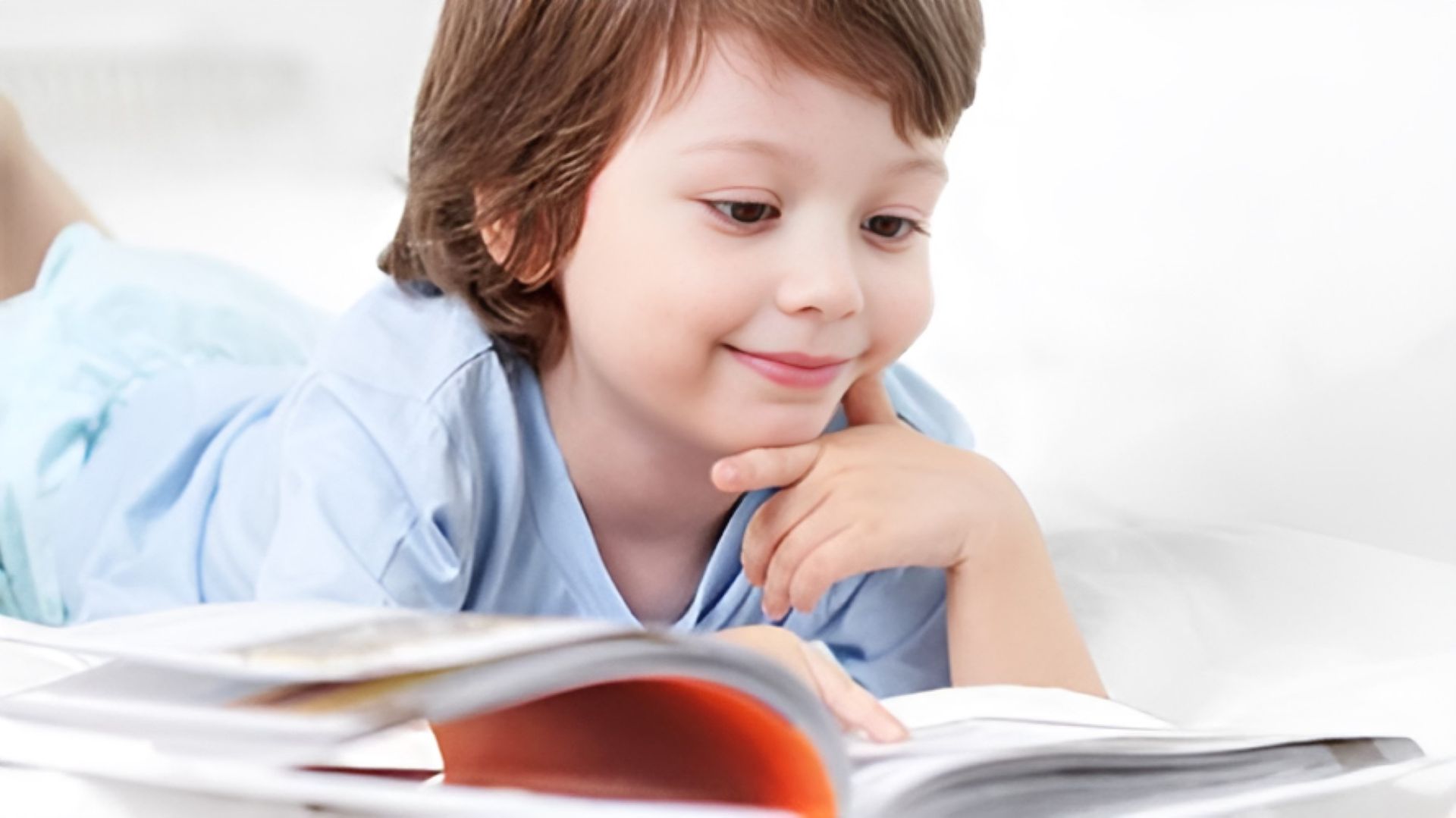 A Young Boy is Laying on His Stomach Reading a Book — Newcastle Paediatric Occupational Therapy in Swansea, NSW