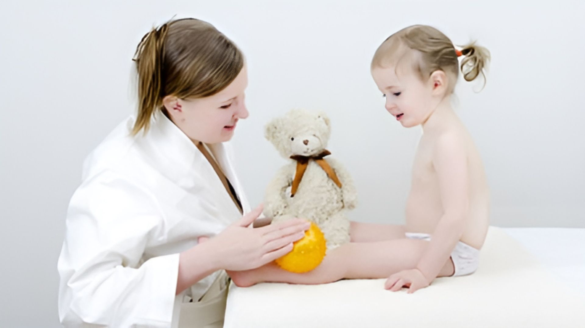 A Doctor is Playing With a Little Girl and a Teddy Bear — Newcastle Paediatric Occupational Therapy In Floraville, NSW