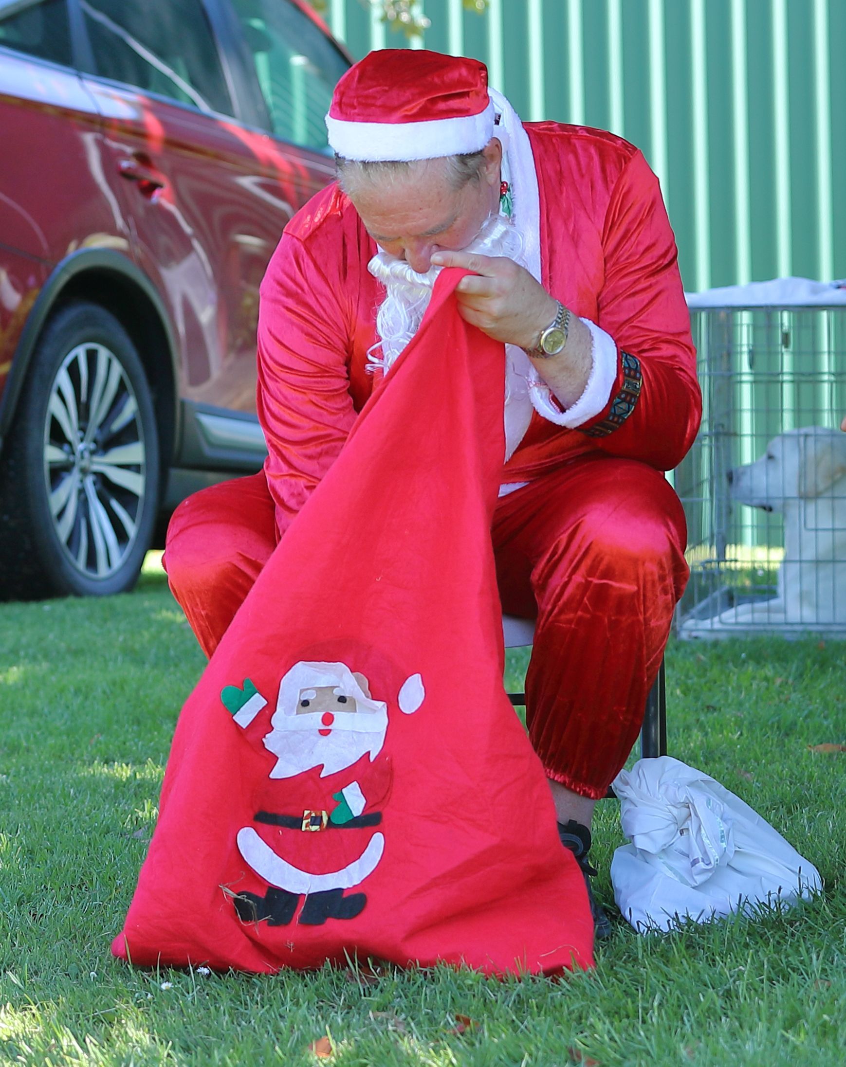 Santa Claus looking inside a red sack decorated with a Santa Claus figure.