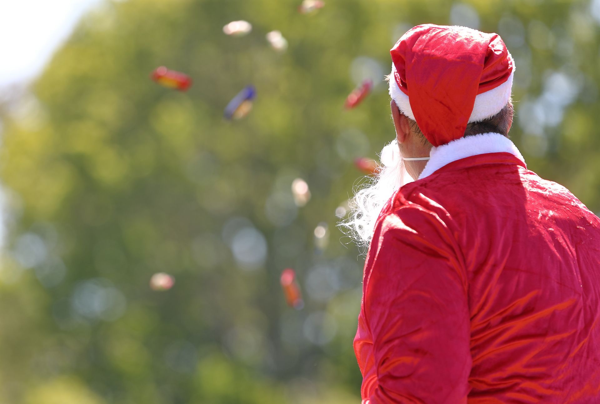 Santa Claus, in red suit, tossing treats in the air, outdoors.