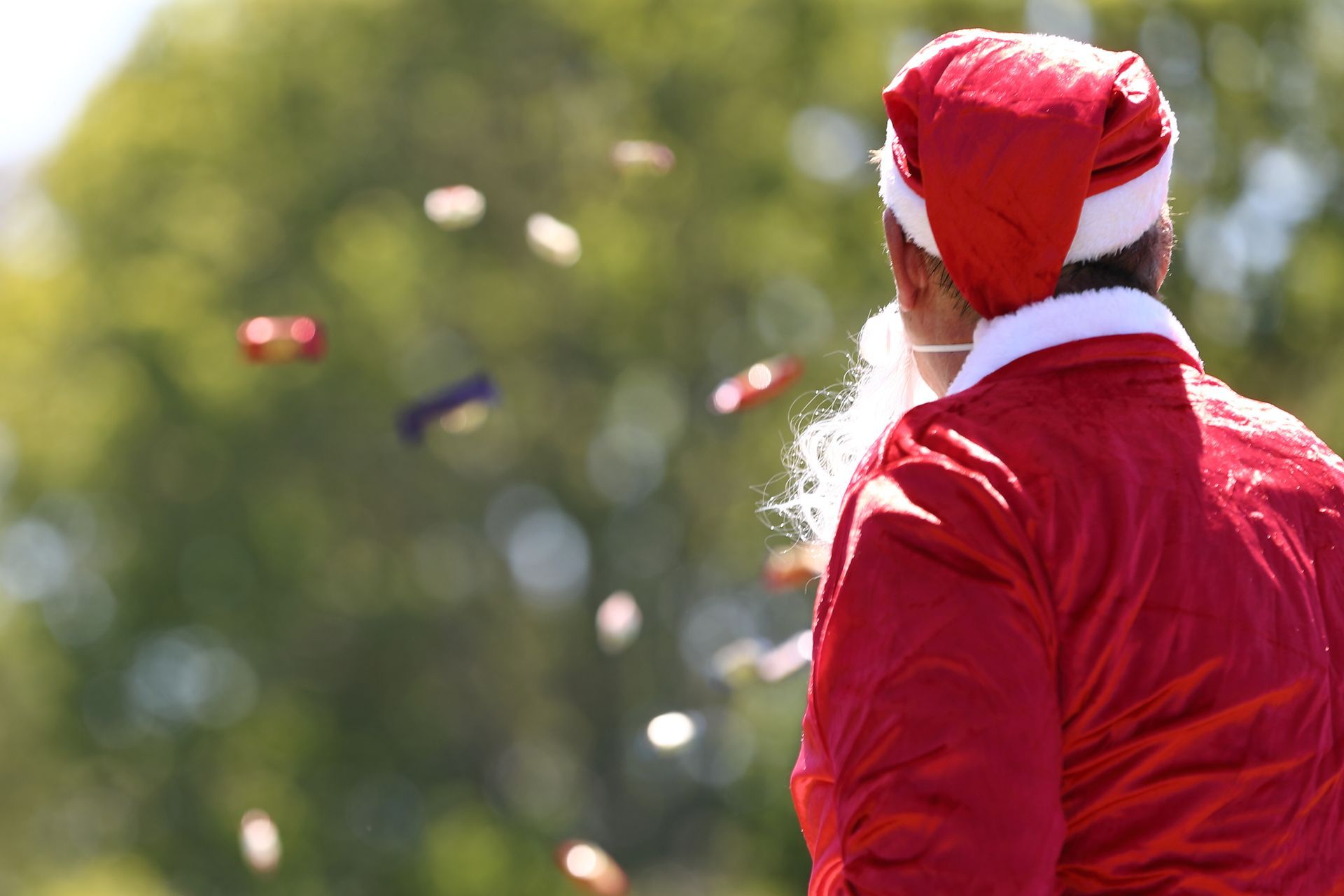 Santa Claus figure throwing objects outdoors. Red suit, white beard, objects in air.