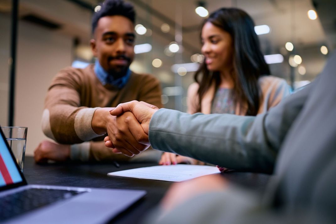 A man and a woman are shaking hands while sitting at a table.