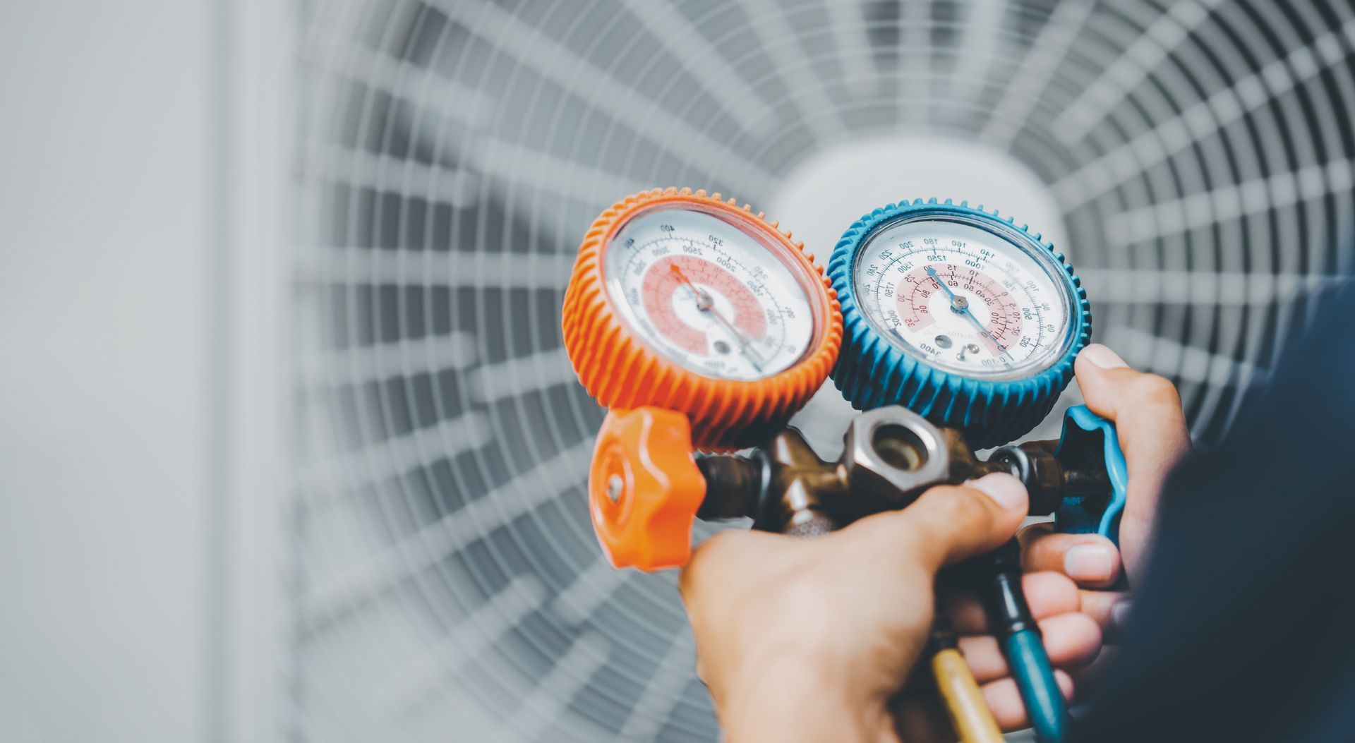 A person is holding two gauges in front of an air conditioner.