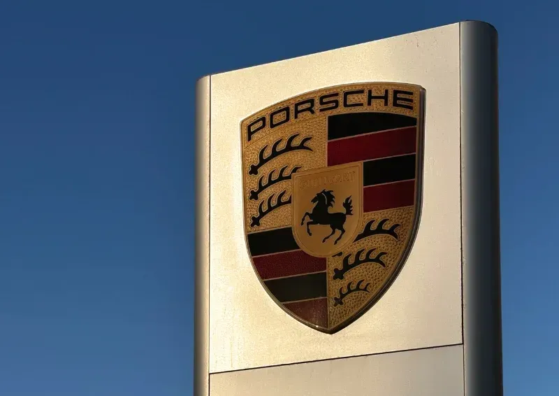 Porsche crest on a tall metallic sign against a blue sky