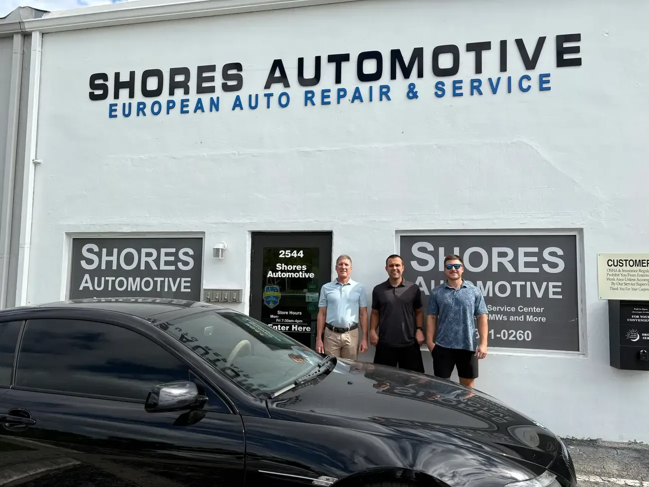 Four people standing outside Shore’s Automotive repair shop, smiling in front of the open garage.