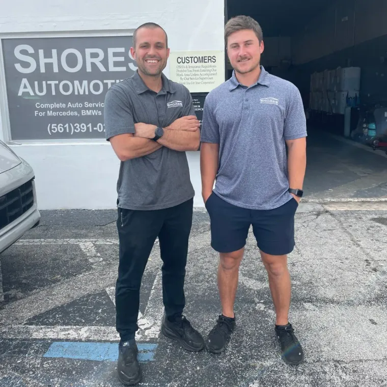 Two men standing outside Shore Automotive, smiling with arms crossed.