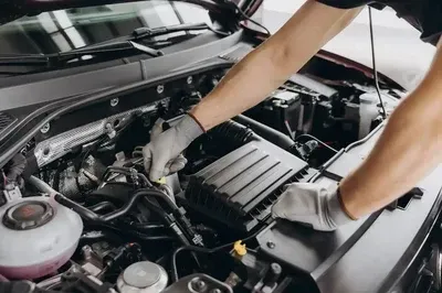 Mechanic working under a car hood, adjusting engine components with gloved hands