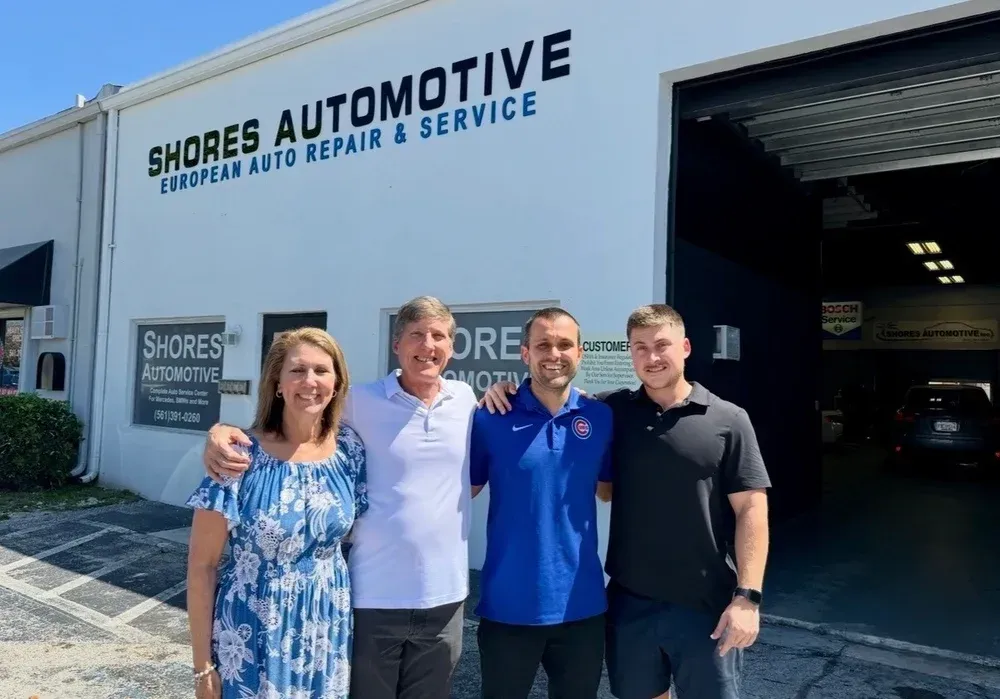 Four people standing outside Shore’s Automotive repair shop, smiling in front of the open garage.