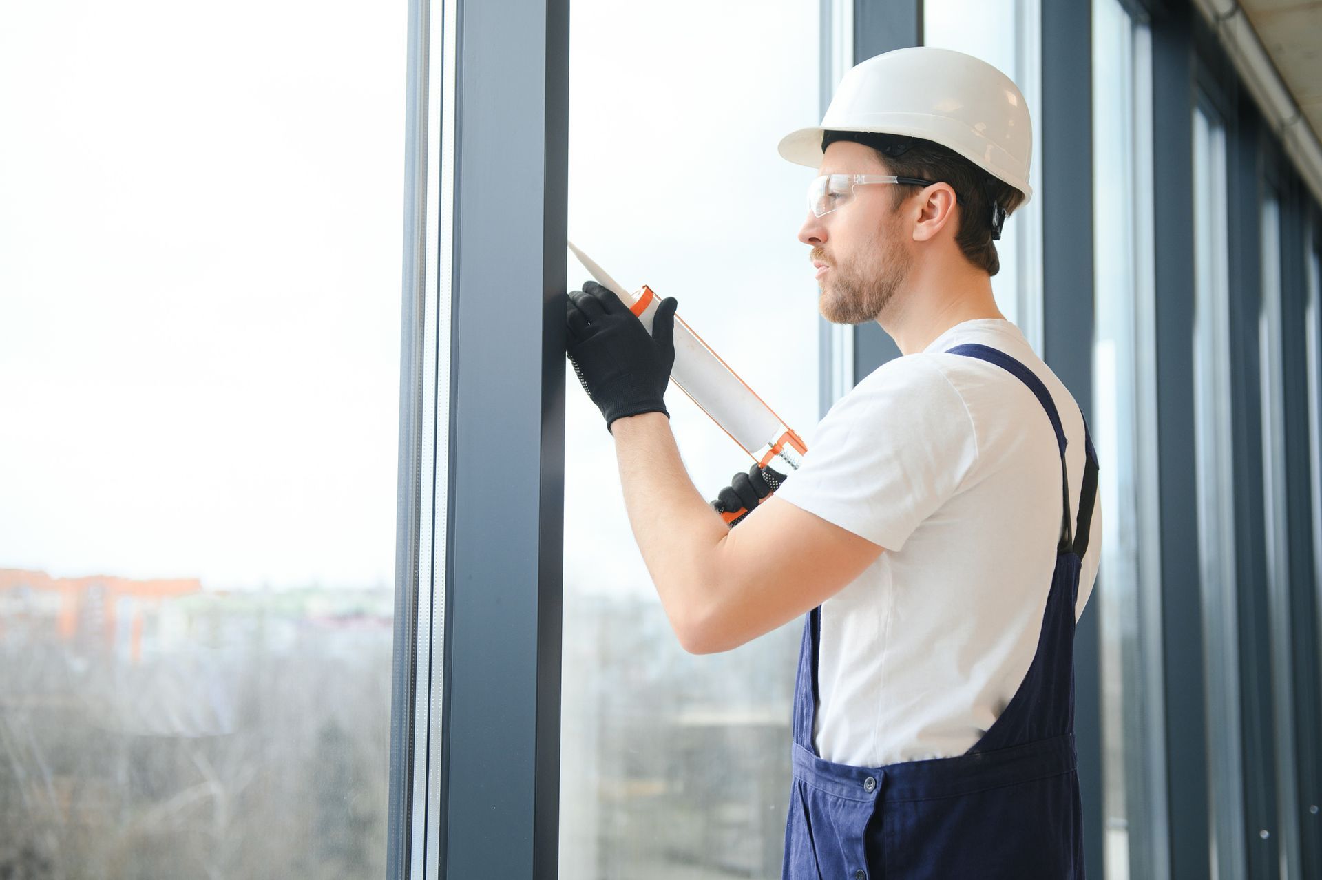 Construction worker in white hard hat caulking a window frame.