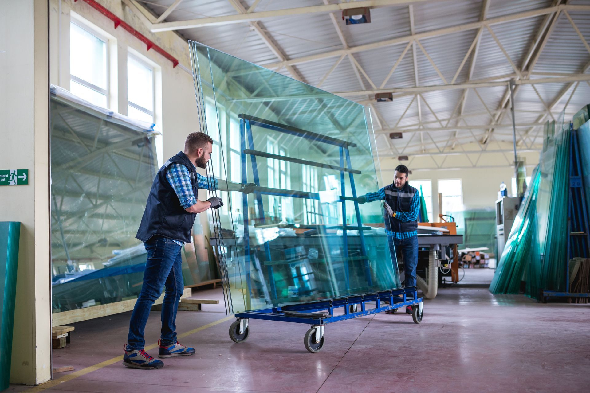Two men moving large glass sheets on a cart in a warehouse.