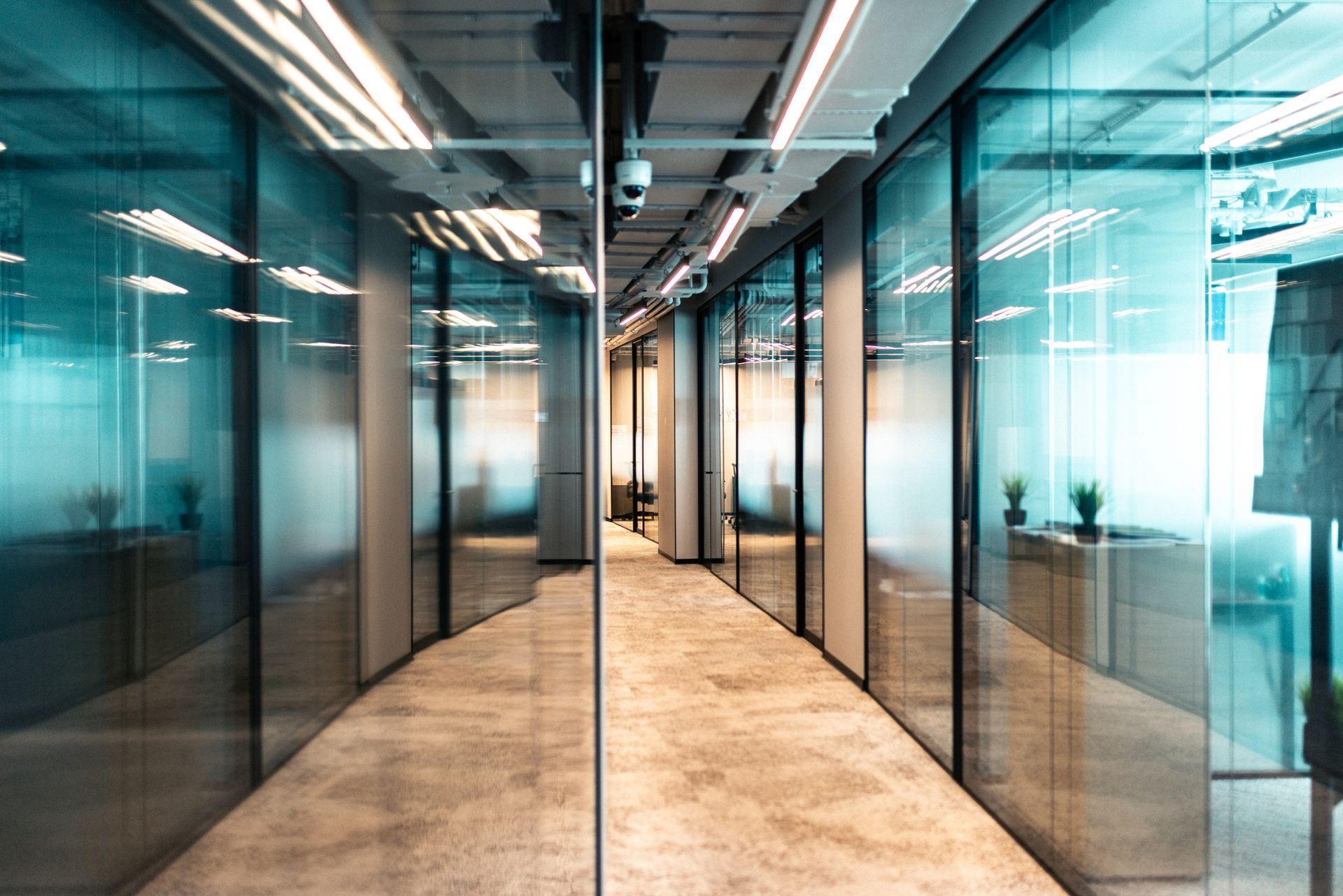 Modern office hallway with glass walls, concrete floor, and overhead lighting.
