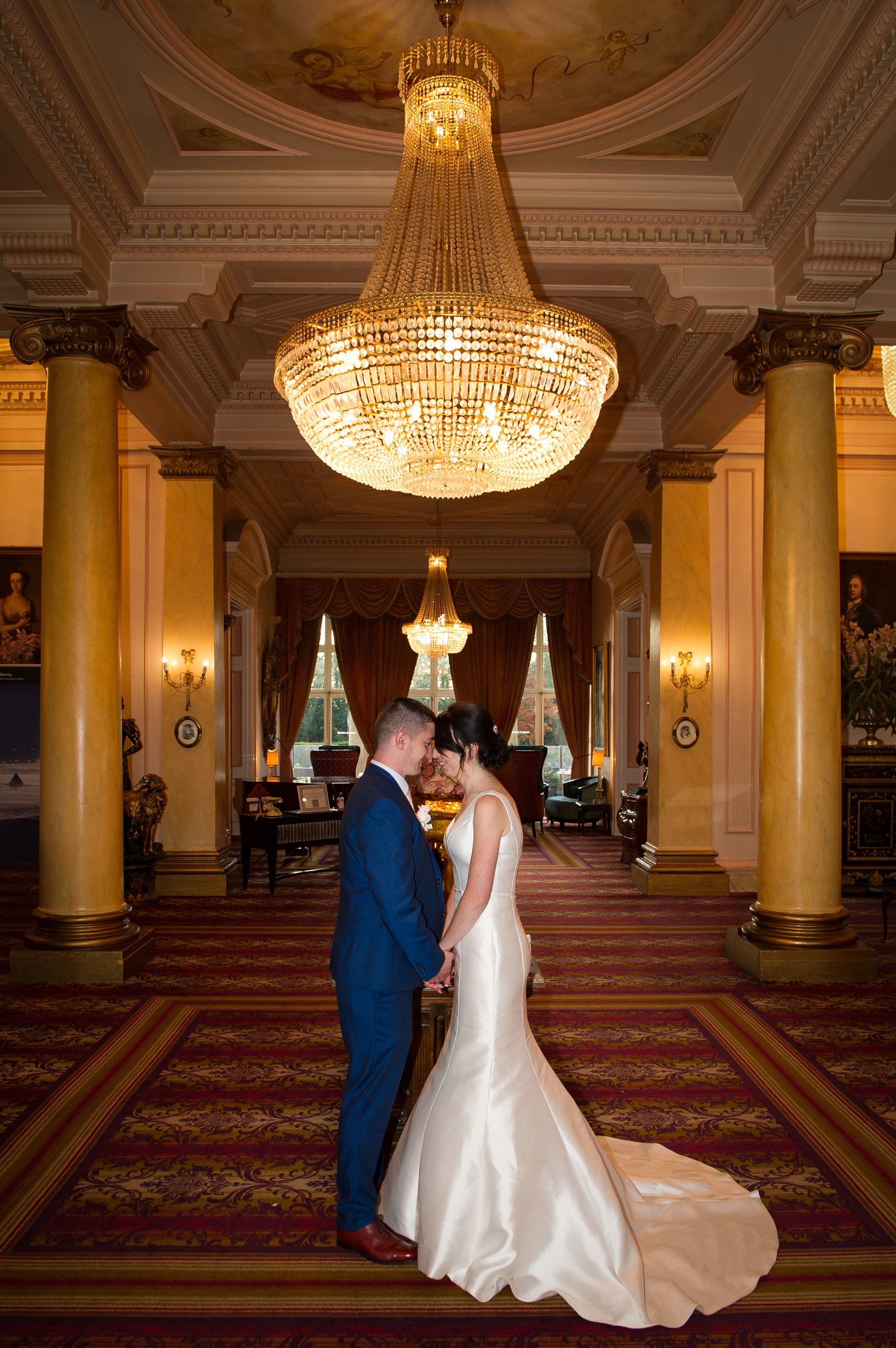 bride and groom holding hands, and looking into each others eyes as they stand under a beautiful chandelier