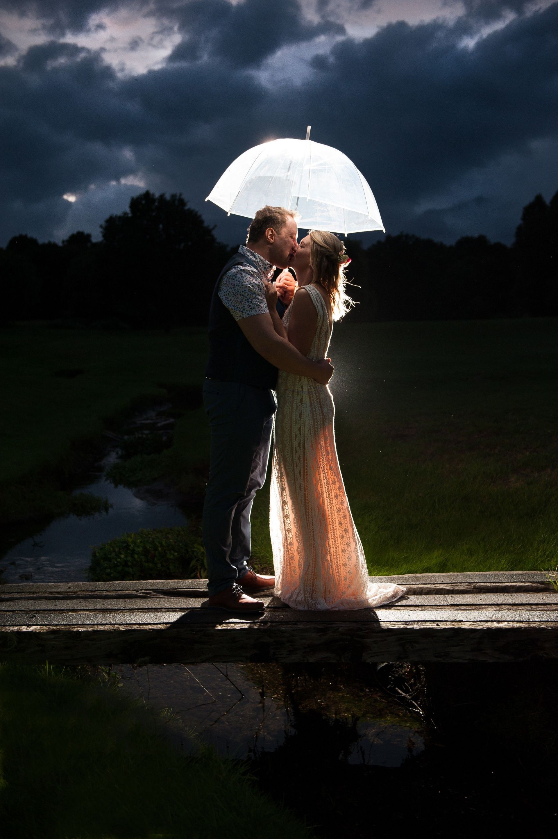 Bride and Groom kissing underneath an umbrella at night with a dark stormy sky