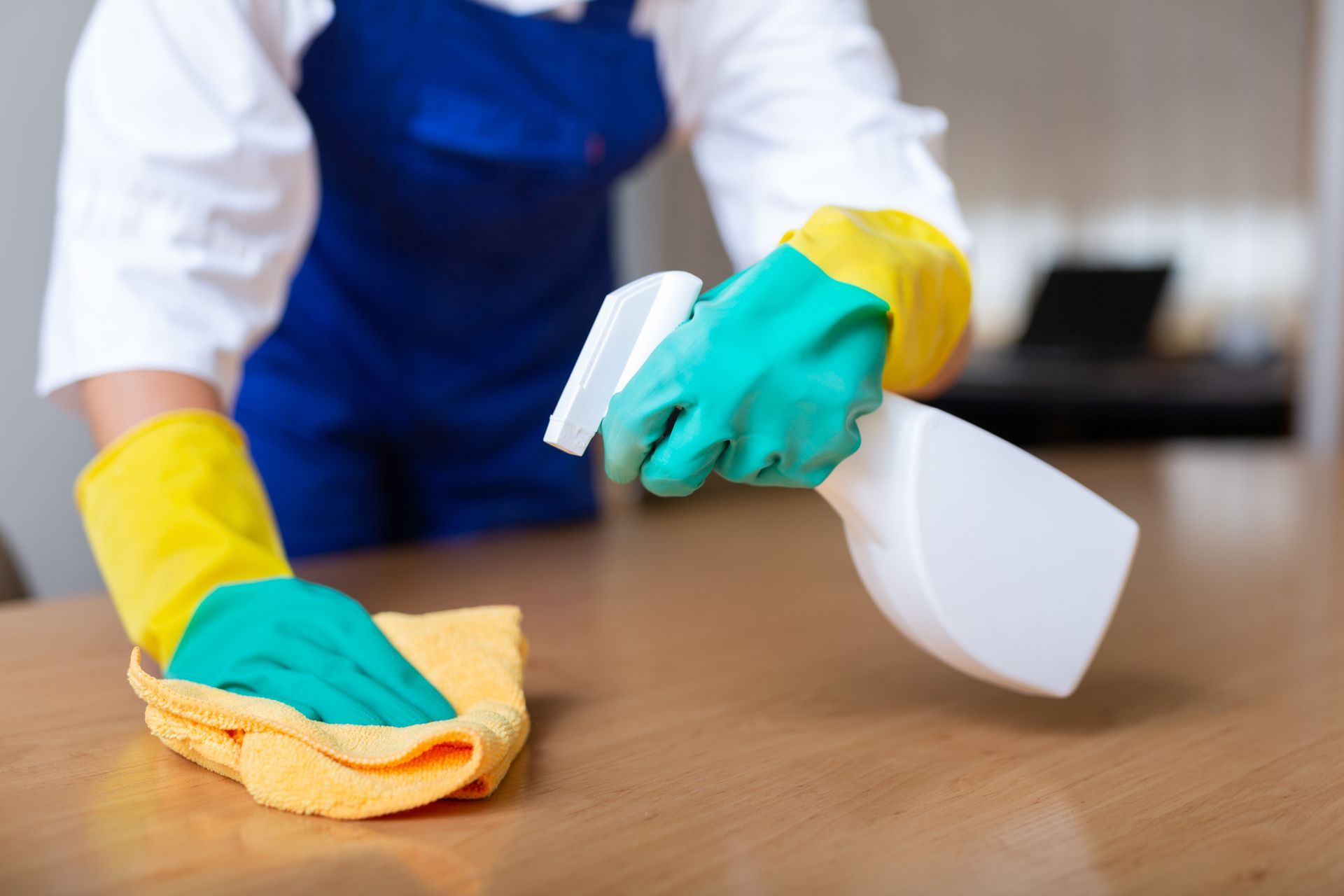 Hands in rubber gloves performing move in cleaning on a wooden table surface.