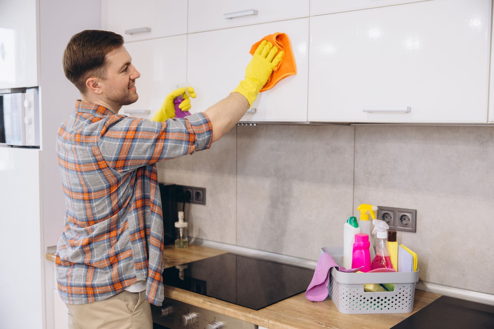 Housekeeper wearing gloves cleaning kitchen cabinets.