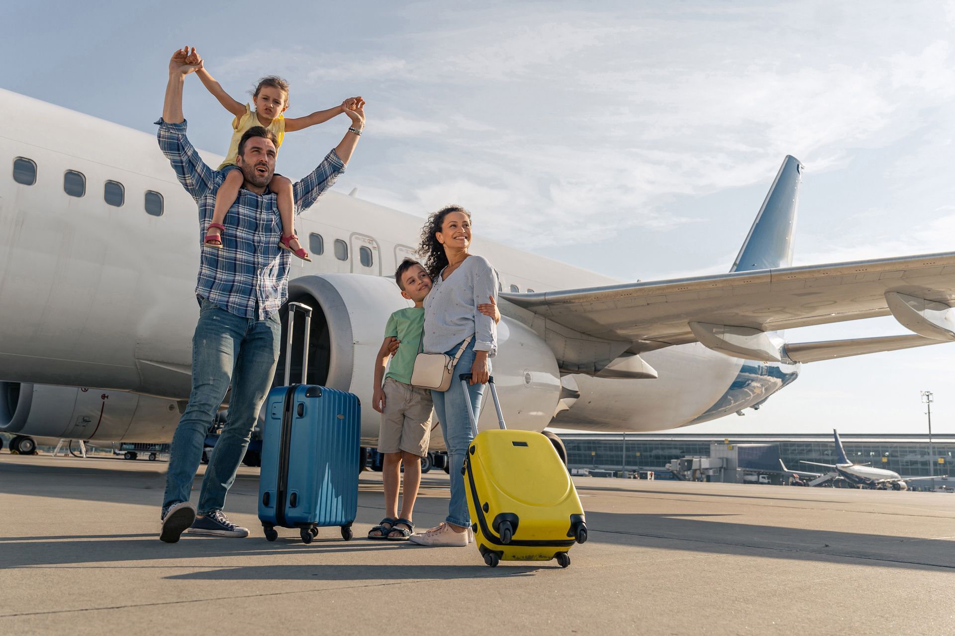 A family with luggage is standing in front of an airplane.