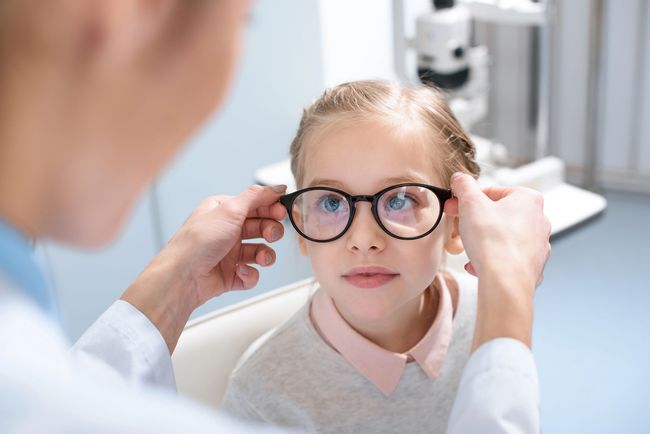 Esame della vista di un bambino con occhiali rotondi, mentre l'optometrista ne regola la montatura.
